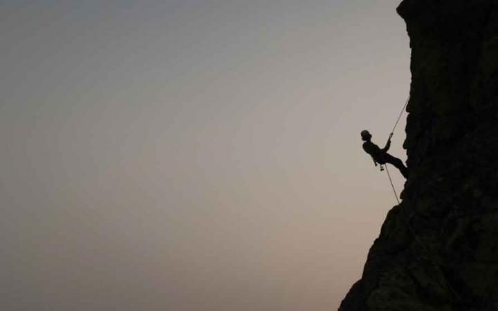 the silhouette of a rock climber resting midway up a rock wall